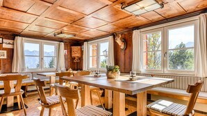 A wooden dining area with a large table and chairs, a mounted animal head, and large windows with curtains.