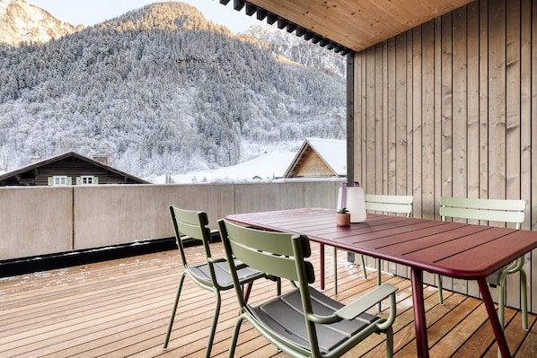 A wooden deck with a table and chairs, overlooking a snowy mountain landscape.