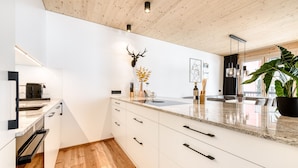 Una cocina moderna con armarios blancos, techo de madera y una isla grande con fregadero.