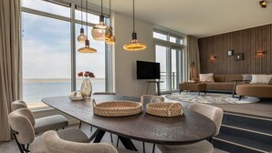 Uma sala de estar moderna com uma janela grande, uma área de refeições com mesa de madeira e um conjunto de sofás.