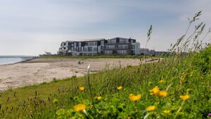 Um edifício moderno com vários andares e janelas amplas, localizado na praia com vista para o mar.