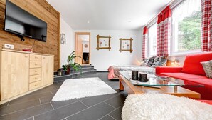 A modern living room with a flat-screen TV, wooden cabinetry, a red sofa, and a glass coffee table. - Appartement Alpenrose (Brand)