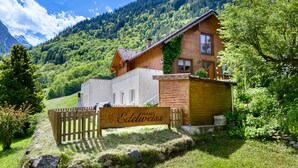 A wooden chalet with a sign reading "Haus Edelweiss" in a mountainous area with lush greenery and a clear sky. - Appartement Alpenrose (Brand)