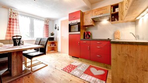 A modern kitchen with red cabinets, a wooden dining table, and a red and white patterned rug. - Appartement Alpenrose (Brand)