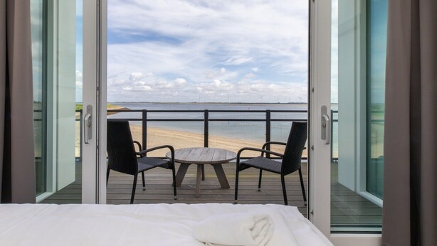 Varanda com mesa, cadeiras, uma cama e vista para a praia e o oceano.