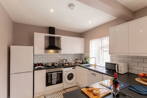 Une cuisine moderne avec des meubles blancs, une hotte noire, un lave-linge et un four à micro-ondes.