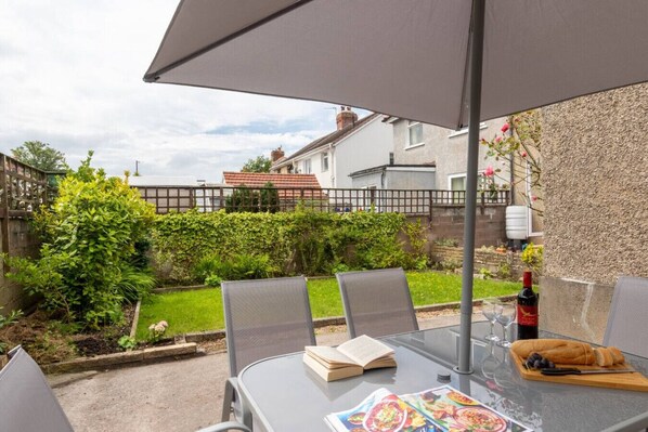 Une terrasse extérieure avec une table, des chaises, un livre, une bouteille de vin et un menu.