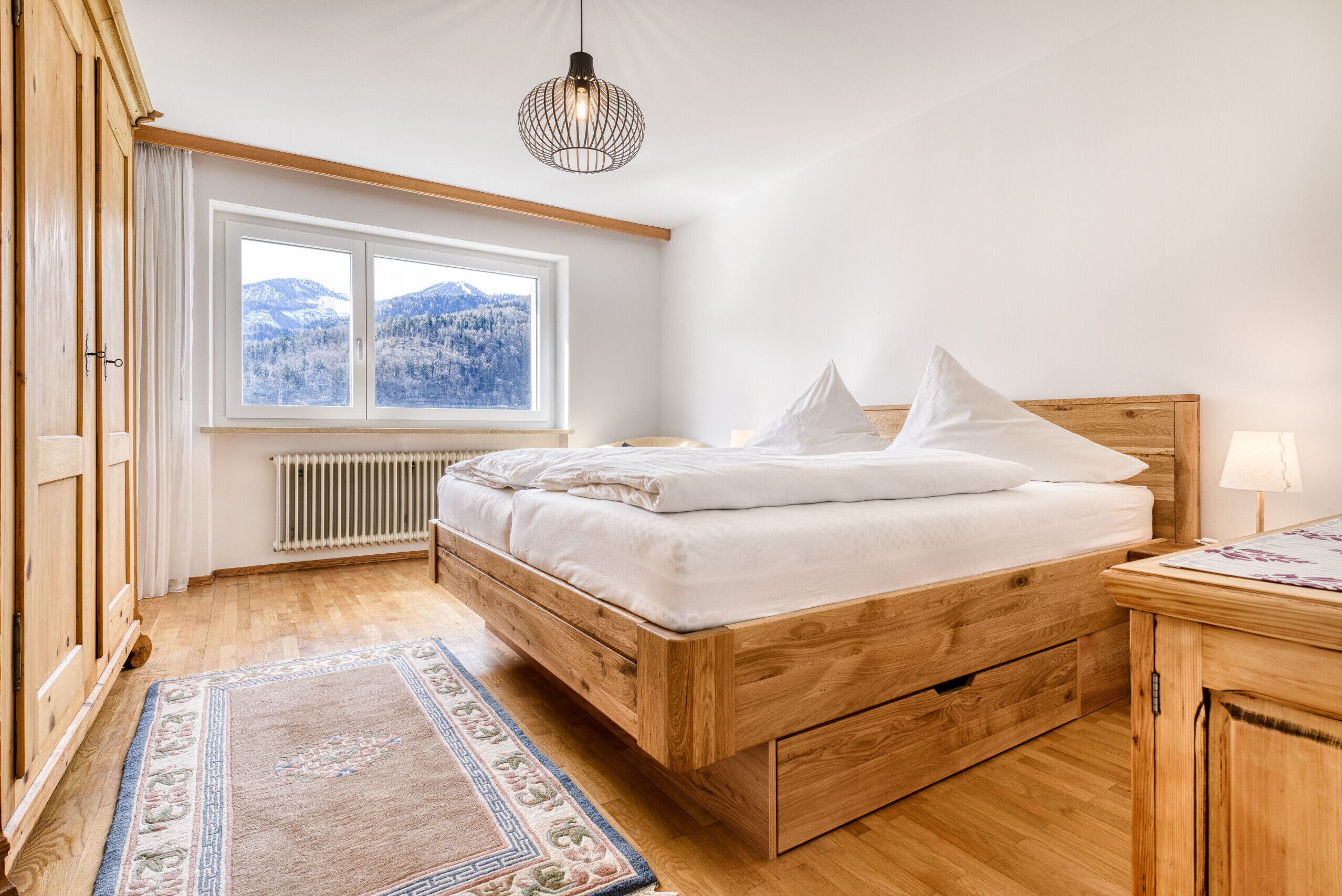 Una camera da letto con un letto di legno, una finestra vista montagna, un termosifone e un'armadio di legno.
