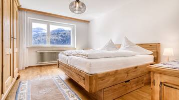 Una camera da letto con un letto di legno, una finestra vista montagna, un termosifone e un'armadio di legno.