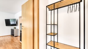 Une chambre moderne avec un plancher en bois, une armoire, un téléviseur fixé au mur et une étagère en métal noir dotée de tablettes en bois.