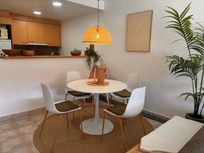 Een eethoek met een ronde tafel, vier stoelen, een hanglamp en een potplant.