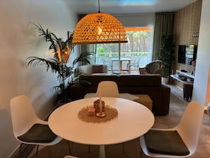 Ein Essbereich mit einem runden Tisch, vier Stühlen, einer Hängeleuchte und einer Couch im Hintergrund.