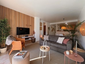 Un salon moderne avec un canapé, un téléviseur, une petite table et une plante en pot.