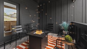 A modern outdoor seating area with a fire feature, black metal chairs, and a decorative plant.