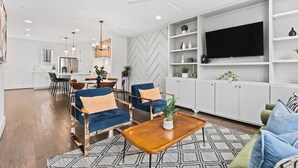 A modern living room with a sofa, coffee table, and TV. There is a dining area with chairs and a table.