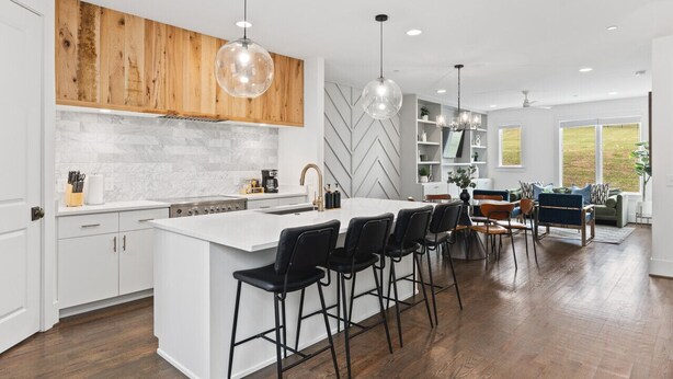 A modern kitchen with a central island, bar stools, wooden cabinets, and pendant lighting.