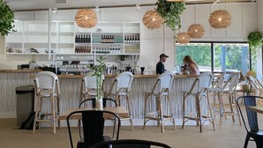 A bar area with wicker chairs, a counter with bottles, and hanging wicker lamps.