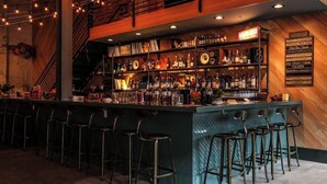 A bar area with a long counter, multiple stools, and a variety of bottles and glasses.