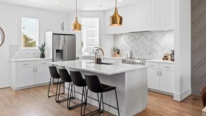 A modern kitchen with white cabinetry, a central island with bar stools, stainless steel appliances, and pendant lighting. - Stunning Home with Garage, Patio - Walk to Restaurants & Coffee (Nashville)