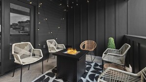 A modern outdoor seating area with wicker chairs, a central fire feature, and a view through a large window. - Stunning Home with Garage, Patio - Walk to Restaurants & Coffee (Nashville)