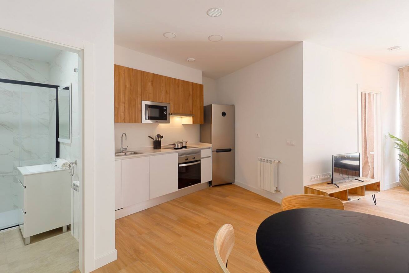 A modern kitchen with white cabinets, a microwave, a refrigerator, and a dining area with a table and chairs.