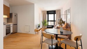 A modern kitchen with a dining area, wooden flooring, and a large window with curtains. - Apartamentos Aptio 644C3 (Oviedo)