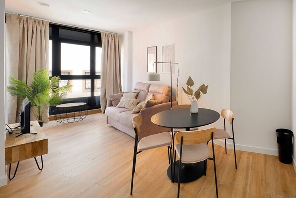 A modern living room with a sofa, a round table with chairs, a floor lamp, and a potted plant.