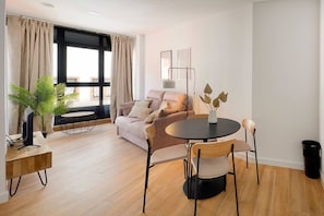 A modern living room with a sofa, a round table with chairs, a floor lamp, and a potted plant.