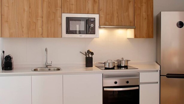 A modern kitchen with wooden cabinets, a microwave, a sink, a stove, and a dishwasher. - Apartamentos Aptio 644C3 (Oviedo)