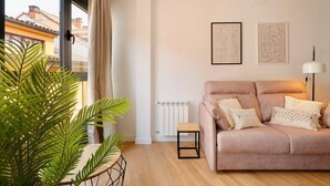 A living room with a sofa, a small table, a radiator, and two abstract paintings on the wall. - Apartamentos Aptio 644C3 (Oviedo)