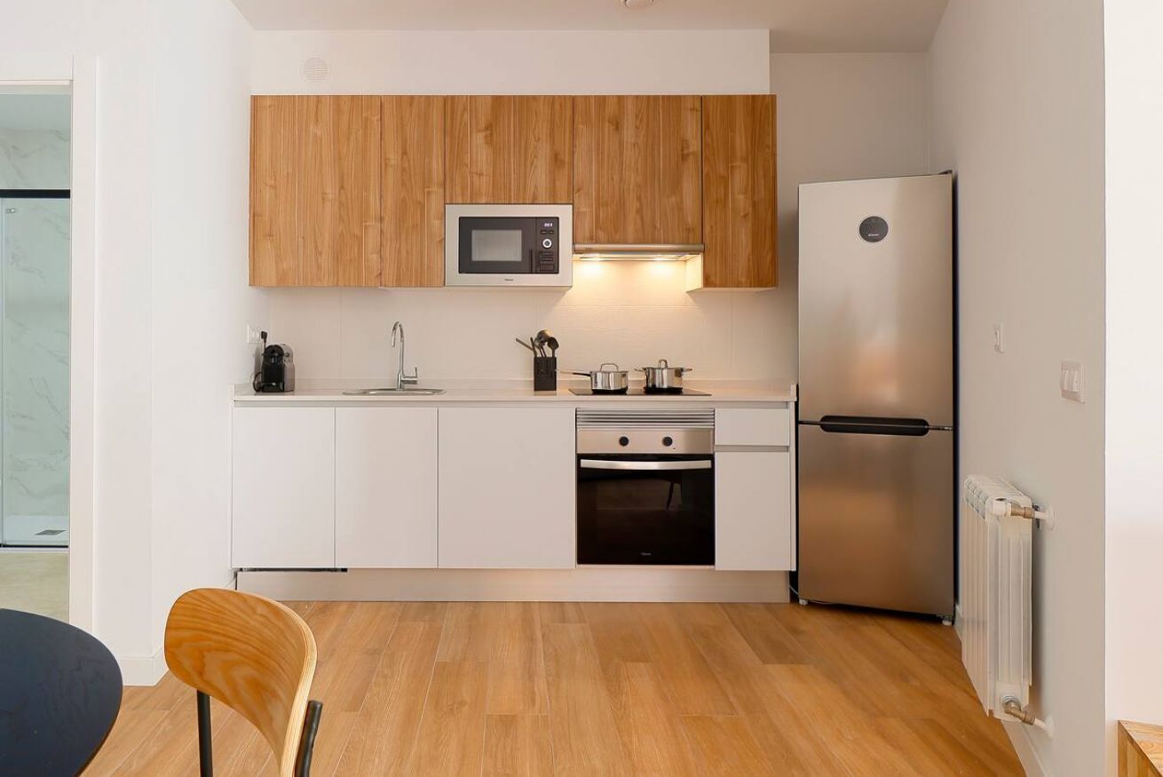 Una cocina compacta con alacenas blancas, microondas, refrigerador de acero inoxidable y lavavajillas.