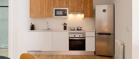 Una cocina compacta con alacenas blancas, microondas, refrigerador de acero inoxidable y lavavajillas.
