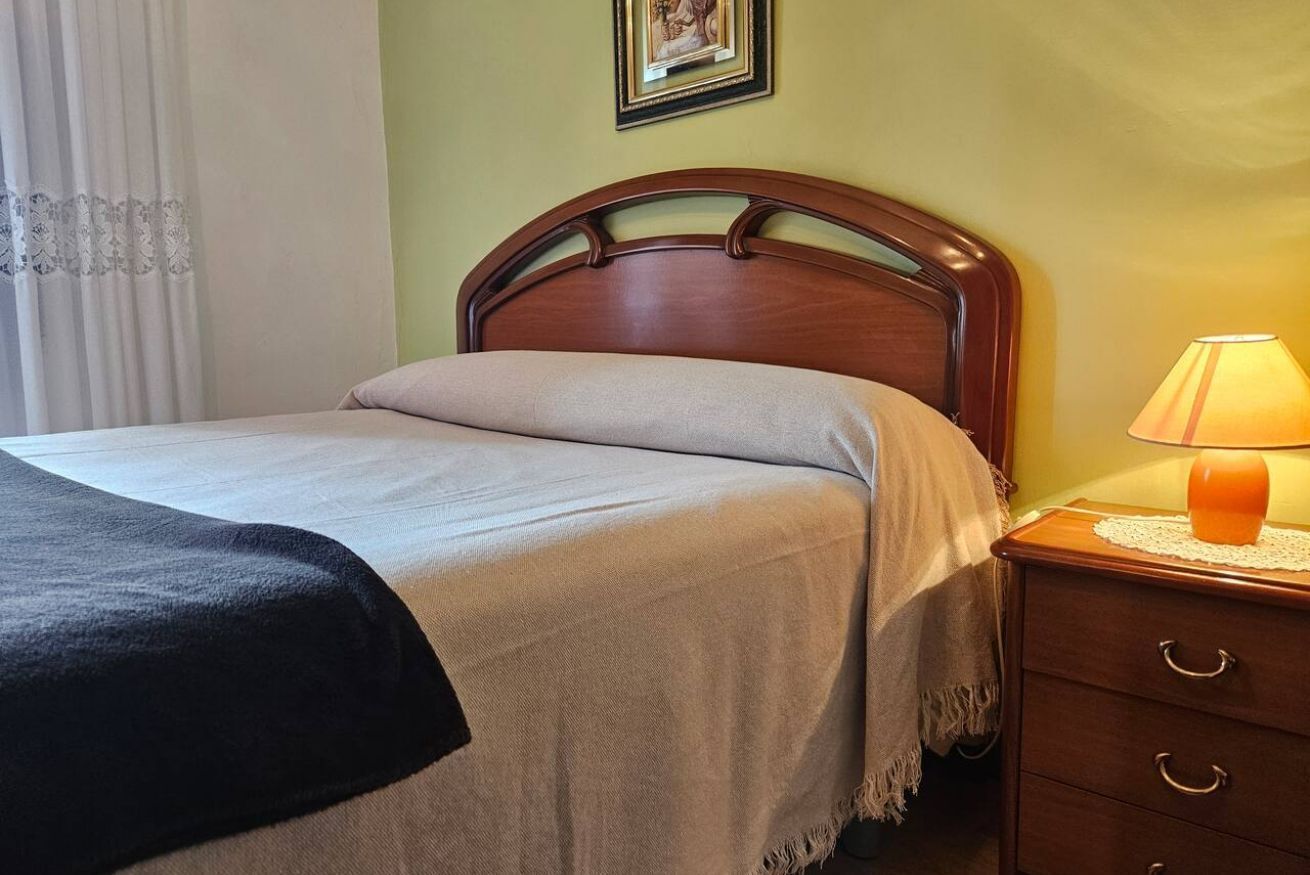 Uma cama com cabeceira de madeira, luminária de cabeceira e mesa de cabeceira com gavetas.