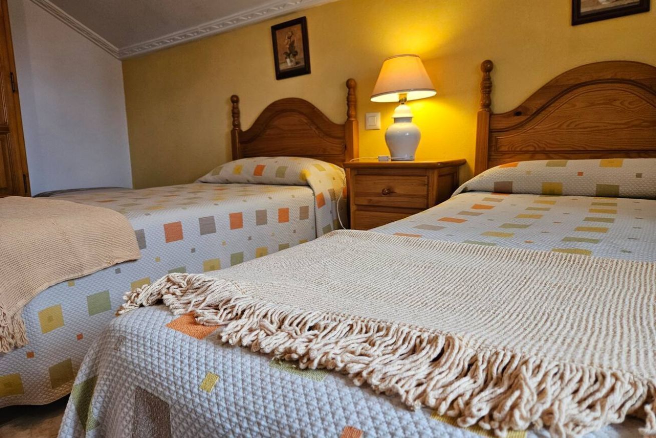Een hotelkamer met twee bedden, een nachtkastje met een lamp en een aan de muur hangend schilderij.
