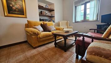 A living room with a sofa, armchair, coffee table, bookshelf, and a painting on the wall.