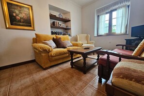 A living room with a sofa, armchair, coffee table, bookshelf, and a painting on the wall.