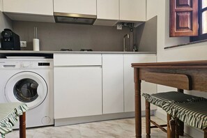A compact kitchen with a washing machine, a coffee maker, and a wooden bench.