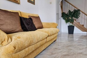 A yellow sofa with brown and black cushions, a potted plant, and a staircase.
