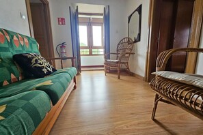 Una habitación con sofá, una silla, piso de madera y una puerta que da al exterior.