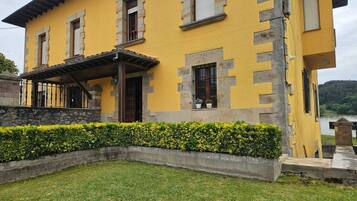 A yellow building with stone accents, a covered porch, and a well-maintained hedge.