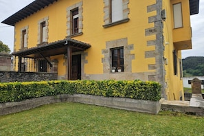 A yellow building with stone accents, a covered porch, and a well-maintained hedge.