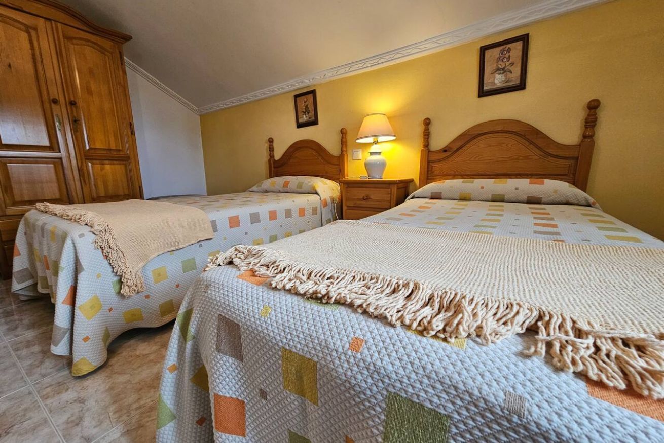 Un dormitorio con dos camas, un armario de madera, una mesita de noche con una lámpara y un cuadro colgado en la pared.