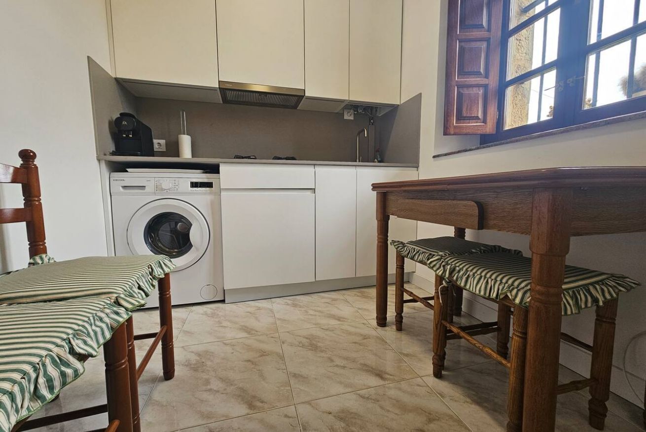 A compact kitchen with a washing machine, a wooden dining table, and chairs.