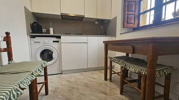 A compact kitchen with a washing machine, a wooden dining table, and chairs.