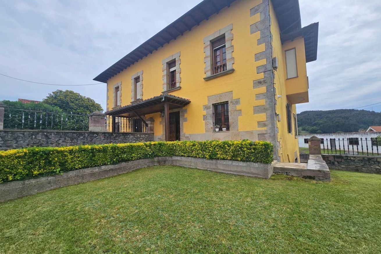 A yellow building with a stone facade, a covered porch, and a well-maintained lawn.