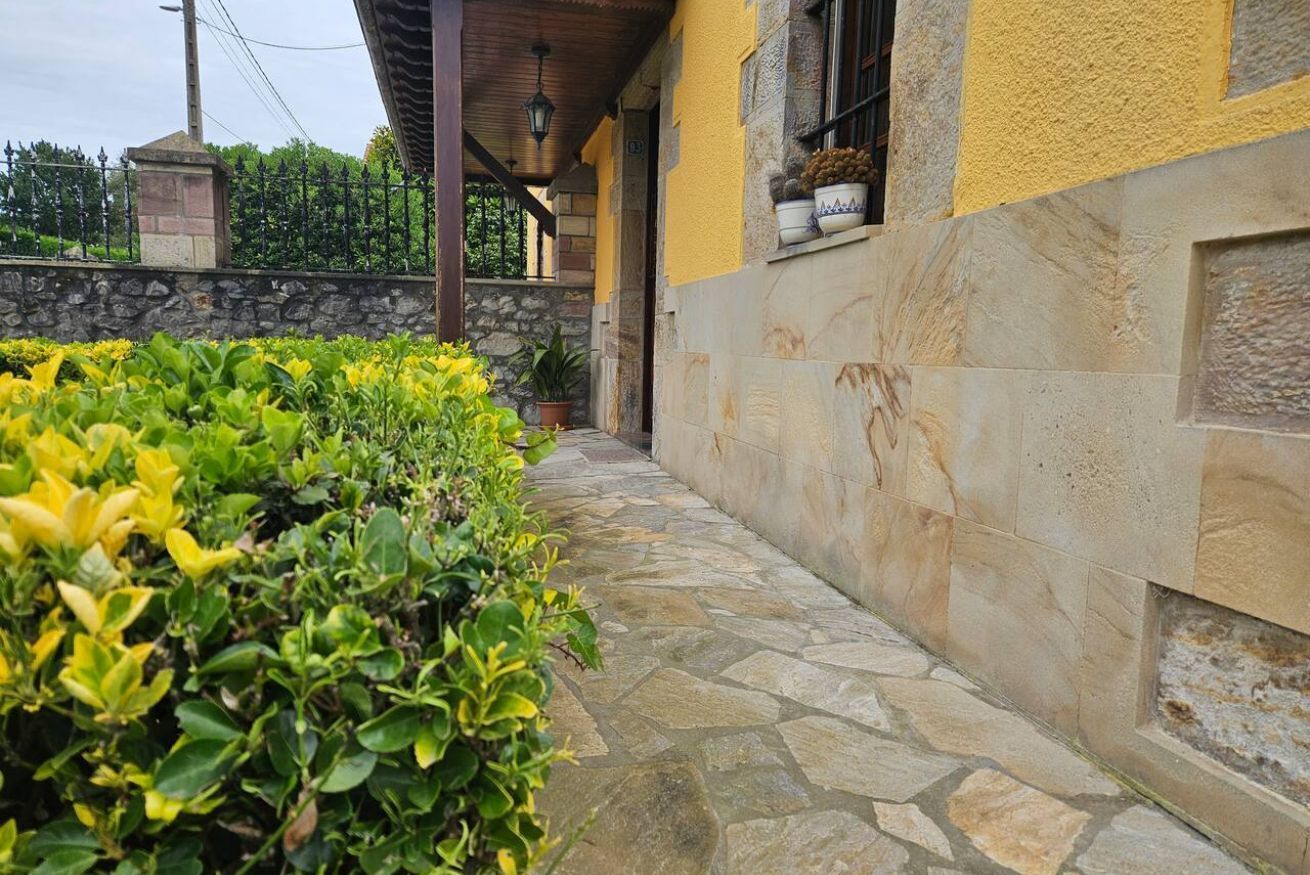 Un camino de piedra que lleva a un edificio con fachada amarilla y una pared de piedra.
