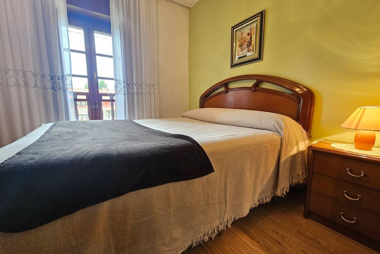 A bed with a wooden headboard, a bedside table with a lamp, and a window with curtains.