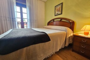 A bed with a wooden headboard, a bedside table with a lamp, and a window with curtains.