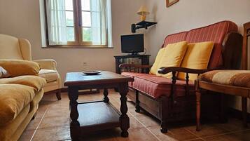 Una sala de estar con sofá, sillón, mesa y televisor.