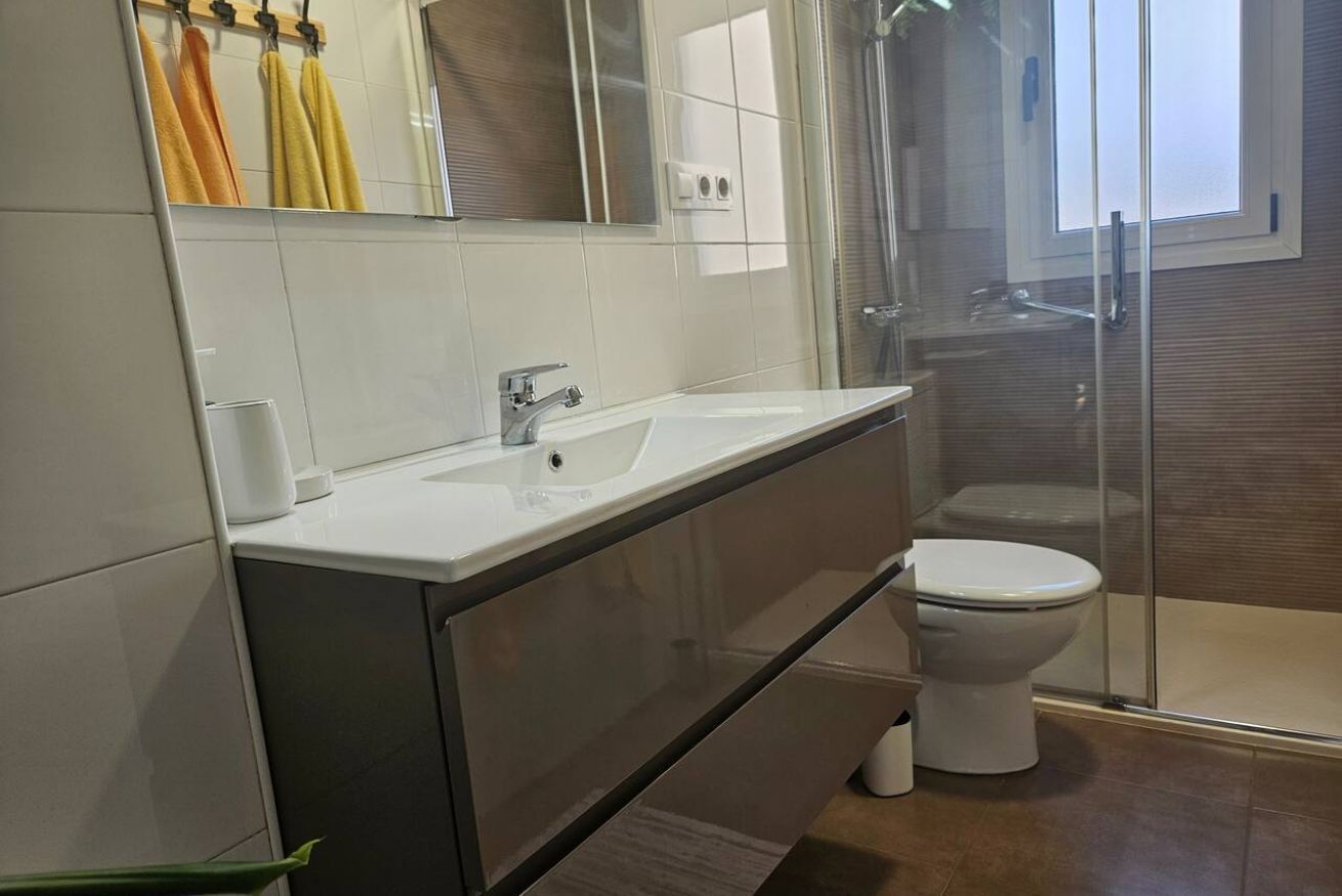Een moderne badkamer met een wit wastafelmeubel, donker kastje en een douchecabine met glazen wanden.